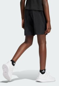 Pantalones cortos deportivos negros de corte holgado y textura suave, combinados con zapatillas blancas y calcetines negros hasta el tobillo.