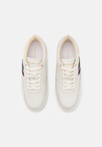 Hvite lærsneakers med beige snøring, polstret innside og en marineblå-rød stripe på siden. Gulllogo på tungen.