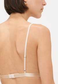 Nude bra with adjustable straps, textured fabric, and a simple hook closure at the back. Minimalist design with no embellishments.