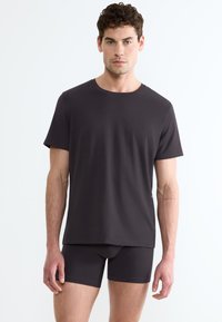 T-shirt grigio scuro con colletto a giro e maniche corte abbinato a pantaloni corti aderenti, realizzati in un tessuto liscio ed elastico.