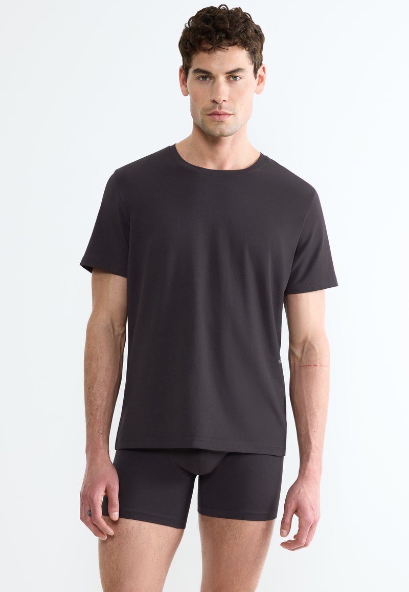 T-shirt grigio scuro con colletto a giro e maniche corte abbinato a pantaloni corti aderenti, realizzati in un tessuto liscio ed elastico.