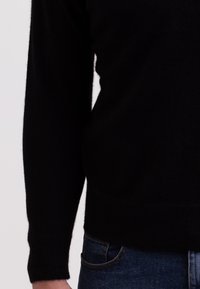 Maglione nero a maglia con maniche lunghe, texture morbida e scollatura rotonda. Abbinato a jeans in denim blu scuro con tasche laterali.