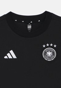 Μαύρο μπλουζάκι από βαμβακερό jersey με ριμπέ κολάρο, με λευκό λογότυπο Adidas και κέντημα της Γερμανικής Ποδοσφαιρικής Ομοσπονδίας με τέσσερις αστέρες.
