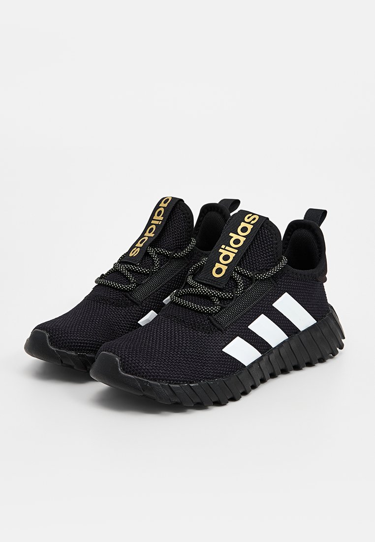 Zwarte gebreide sportschoenen met een gestructureerde bovenkant, witte drie strepen en een gouden logo-detail op de tong; rubberen zool met een gegroefd patroon.
