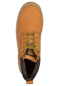Bota de tobillo de cuero marrón claro con cordones amarillos, suela de goma y un forro acolchado marrón. Presenta ojetes metálicos y detalles cosidos.