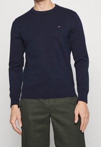 Marineblauer Strickpullover mit Rundhalsausschnitt, langen Ärmeln, gerippten Bündchen und Saum, mit einem kleinen dreifarbigen Logo auf der Brust.