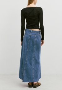 Schwarzes Langarmshirt mit gerippter Textur, kombiniert mit einem hochgeschnittenen, hellblauen Jeansmaxikleid mit seitlichen Nähten und raw Saum. Braune Schuhe.