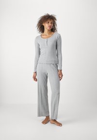 Pyjama gris en ribbed avec un haut à manches longues, doté d'un col rond et de trois boutons, associé à un pantalon à jambes larges. Les bords ont une finition en dentelle.