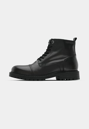 Black leather ankle boots with round toe, lace-up design, contrasting gray eyelets, and rugged rubber outsole. Smooth texture with minimal accents.