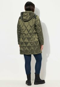 Olivgrön isolerad jacka med huva, med en diamantquiltad design, långa ärmar och medellång skärning, som är ihopparad med mörka jeans och stövlar.
