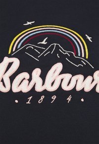 Vyšívaná modrá textilie s motivem hor, nad nimiž se klene duha, a slovo "Barbour" napsané růžově. Obsahuje bílé ptáky a číslo "1894" níže.