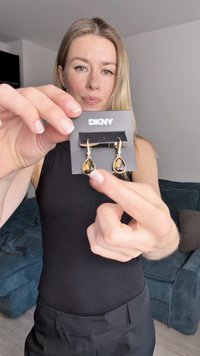 DKNY dråpendroppeøreringer i gulltone med dråpeformet brun edelsten, hengende på et svart kort. Vist mot en nøytral bakgrunn.