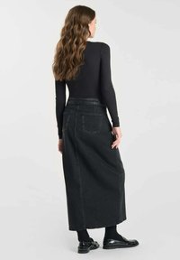 Zwarte denim maxi-rok met een rechte snit, achterzakken en gestikt detail. Gecombineerd met een strakke lange mouw top en zwarte schoenen.