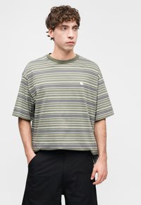 Ριγέ κοντομάνικη μπλούζα σε ελαιί πράσινο, γκρι και λευκό, με στρογγυλή λαιμόκοψη και μικρό λογότυπο στο αριστερό στήθος.