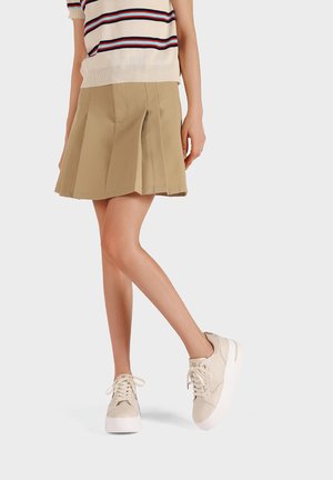 Gonna plissettata beige abbinata a sneakers platform bianche con texture liscia e design con lacci. Maglione a maniche corte a righe sopra.
