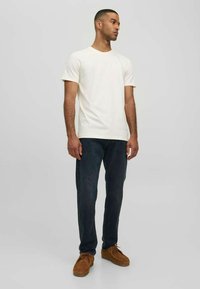 Vit bomulls tröja med rund hals som kombineras med mörkblå jeans och bruna skor. Passformen är avslappnad med en enkel, ren design.