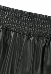 Zwarte leren broek met een gestructureerd oppervlak, voorzien van een elastische taille en een losse pasvorm. Details omvatten verticale naden voor extra ontwerp.
