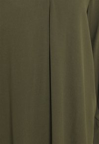 Tissu vert olive avec une texture lisse, présentant un design subtil de pli. Le matériau semble léger et tombe doucement.