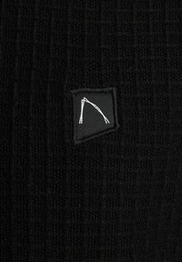 Tessuto nero con una trama a griglia, caratterizzato da una piccola toppa nera ricamata con un design geometrico bianco.
