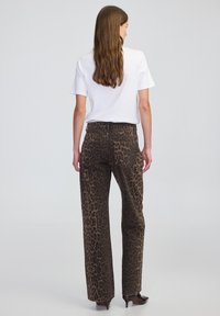 Jeans w szerokich na nogawkach w nadruk panterki na ciemno-brązowym tle, z wysokim stanem i tylnymi kieszeniami, połączone z gładką białą koszulką.