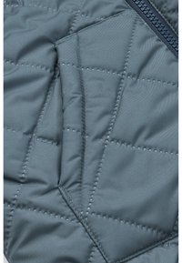 Tessuto trapuntato di un azzurro chiaro con cuciture a forma di diamante e una tasca laterale con zip nascosta. Texture morbida e finitura liscia.