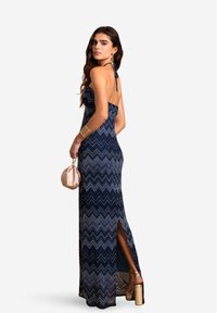 DRESS MAXI CON PATERNO A ZIG-ZAG BLU NAVY CON COLLO HALTER, FENDINA LATERALE E SILHOUETTE ADERENTE, ABBINATO A UNA SOFFICE BORSETTA ROSA E TACCHI DORATI.
