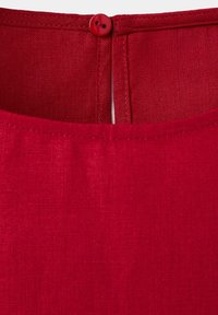 Gros plan d'un col en tissu rouge avec un bord cousu et un petit bouton rouge au dos.