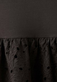 Tissu noir avec une partie supérieure lisse et une partie inférieure présentant une broderie florale texturée et des détails découpés.