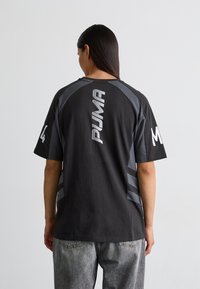Sort T-shirt med korte ærmer og grå detaljer. Har et lodret hvidt "PUMA" logo og nummer "14" på ryggen. Lavet af bomuld, afslappet pasform.