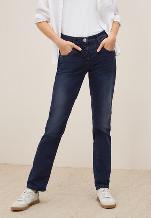 Rechtaflopende donkerblauwe jeans met een vijf-vakken ontwerp, knoopsluiting in de taille en een lichte vervaging op de stof, gecombineerd met witte sneakers.