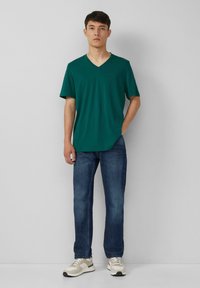 Groene V-hals t-shirt van katoen, gecombineerd met blauwe jeans en lichtgekleurde sneakers. Eenvoudig design met korte mouwen en een relaxte pasvorm.
