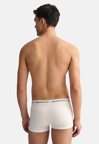 Boxeri din bumbac alb cu un elastic de culoare albastră, prezentat pe un model din spate, punând în evidență textura netedă și croiala.