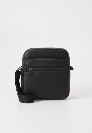 Black leather crossbody bag with a zippered front pocket, adjustable strap, and embossed logo, featuring a smooth texture and simple design.
