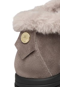 Stivale grigio in suede con un morbido risvolto di pelliccia grigia chiara, caratterizzato da un accento circolare con logo dorato e una superficie texture.