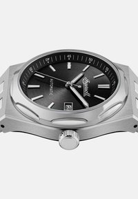 Montre automatique en acier inoxydable avec un cadran noir texturé, des index de heures argentés et un affichage de la date, dotée d'une couronne de remontoir proéminente.