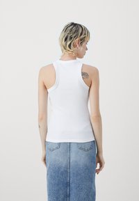 Vit, ribbad, ärmlös linne med rund halsringning; slät textur; bärs med en ljus denimkjol.
