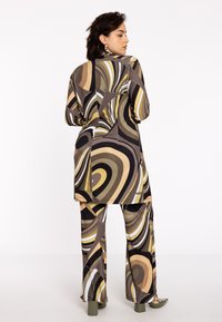 Langärmlige Tunika und ausgestellt geschnittene Hosen in einem mehrfarbigen Wirbelmuster. Der Stoff wirkt glatt; die Farbpalette umfasst Braun, Beige und Oliventöne.