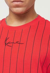T-shirt à manches courtes rayé rouge en coton. Il présente une signature noire brodée sur la poitrine, un col rond et une coupe ajustée.