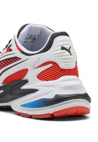 Vista posteriore di una sneaker Puma bianca, rossa e nera con tessuto in rete, suola ammortizzata e etichetta della taglia visibile all'interno.