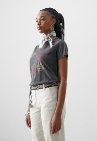 Grå bomullströja med grafisk design, ihopparad med ljusa byxor. Vit scarf runt halsen och mönstrat bälte med flamm detaljer.