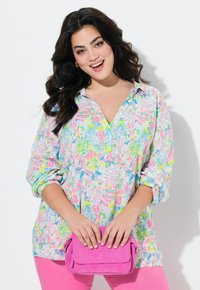 Lichte, kleurrijke shirt met een bloemenpatroon in blauw, roze en groen. Heeft een kraag en opgerolde mouwen. Gecombineerd met een roze corduroy tas.