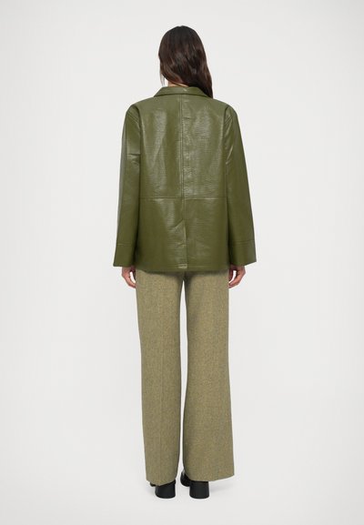 Giacca in finta pelle verde oliva con una vestibilità rilassata, ampi risvolti e dettagli delle cuciture visibili, abbinata a pantaloni a gamba larga grigio a scacchi.