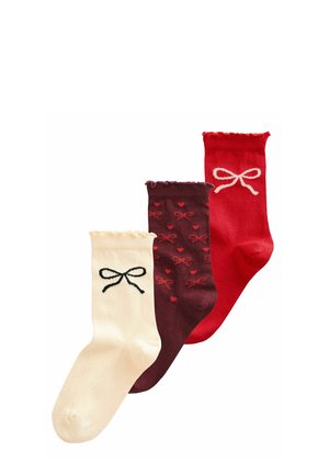 Tri par socks v kremni, burgundski in rdeči barvi. Značilnosti vključujejo skodrane manšete, vzorec s pentljami na burgundski ter črno pentljo na kremni.