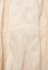Țesătură de culoare bej deschis, cu o textură netedă, având cute subtile. Designul include linii de cusătură pentru detalii și structură suplimentară.