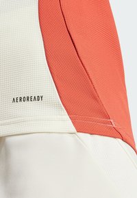 Haut de sport AEROREADY avec des panneaux texturés corail et blancs, présentant des coutures visibles et un tissu respirant pour une gestion de l'humidité.