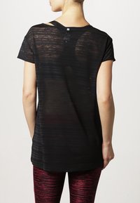 Camisa negra de manga corta con textura semitranslúcida y rayas horizontales, diseño de espalda abierta y un corte relajado.