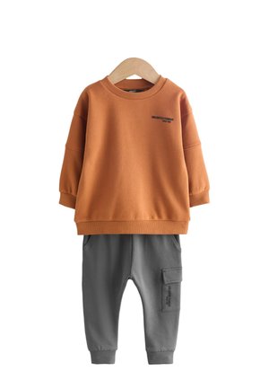 Sweat-shirt orange avec texte noir et pantalon cargo gris. Tissu doux, coupe ample, poignets côtelés et poches sur le pantalon.