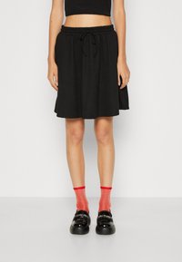 Svart knelengde skjørt med elastisk midjebånd og snorer. Brukt sammen med røde glitrende strømper og skinnende svarte loafers.
