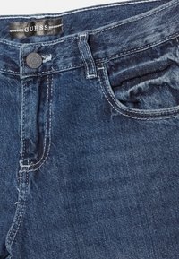 Tmavě modré džínové kalhoty s knoflíkovým a zipovým zapínáním, designem s pěti kapsami a viditelnými švy na látce.