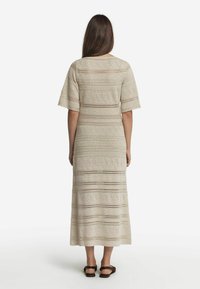 Knee-lång, ljusbeige virkade klänning med korta ärmar, med geometriska mönster och öppet arbete längs nederkanten och kroppen.
